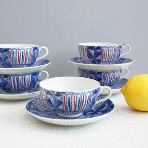 May include: Set of four blue and white teacups and saucers with red accents. The cups and saucers feature a geometric pattern.