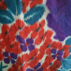 Op de afbeelding: Een close-up van een stof met een kleurrijk bloemenpatroon. De stof is een mix van rood, blauw, paars en wit.