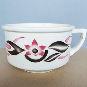 May include: White ceramic mug with a pink and brown floral design. The mug has a rounded shape and a handle.