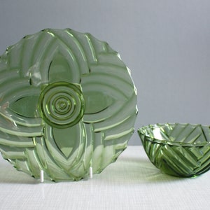 May include: Two green glass bowls with a geometric pattern. The larger bowl has a more intricate design with a central circle and four petals. The smaller bowl has a simpler design with diagonal lines.