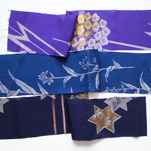 Op de afbeelding: Vijf stroken stof in verschillende tinten blauw en paars met verschillende bloem- en geometrische patronen. De stof is gevouwen en gestapeld.