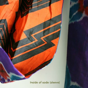 Op de afbeelding: De binnenkant van een traditioneel Japans kledingstuk, genaamd "sode", met een feloranje stof met een zwart geometrisch patroon. De stof is dubbelgevouwen en de buitenkant van het kledingstuk is een paars-blauw tie-dye patroon. De tekst "Inside of sode (sleeve)" is zichtbaar onderaan de afbeelding.