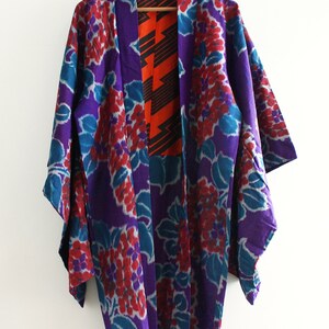 Op de afbeelding: Een paarse en turquoise kimono met een bloemenpatroon. De kimono heeft een rode en zwarte geometrische voering.