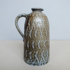 May include: A brown ceramic pitcher with a white glaze and a diamond pattern. The pitcher has a handle and a spout.