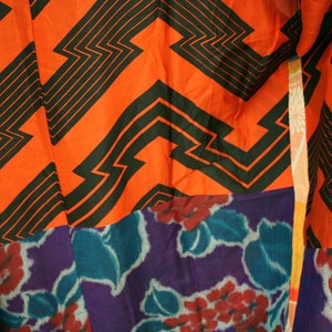 Op de afbeelding: Een kleurrijke stof met een geometrisch patroon in zwart en oranje. De stof is aan elkaar genaaid met een paarse en blauwe bloemenstof.