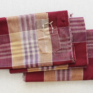 May include: Three pieces of red and tan plaid fabric with a patch sewn on the top piece.