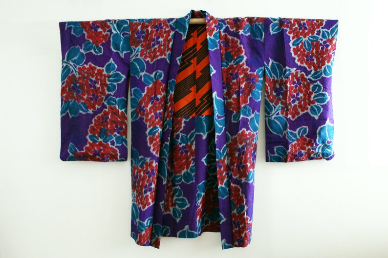 Op de afbeelding: Een paarse en blauwe kimono met een rood en oranje bloemenpatroon. De kimono is gemaakt van zijde en heeft een traditioneel Japans ontwerp.