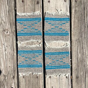 May include: Four gray woven coasters with a blue geometric pattern. The coasters have a frayed edge.