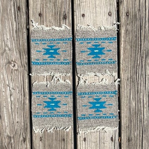 May include: Set of four gray woven coasters with a blue and white geometric pattern. The coasters have a fringed edge.