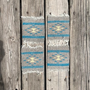 May include: Four gray woven coasters with a blue and yellow geometric pattern. The coasters are on a wooden surface.