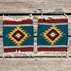 May include: Two small teal blue and yellow woven rugs with geometric patterns. The rugs have a red and white border and fringe.