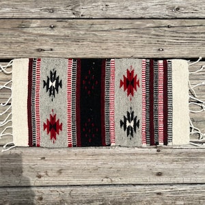 May include: A gray, black, and red woven rug with a geometric pattern. The rug has fringe on the ends.
