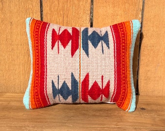 May include: A decorative pillow with a geometric pattern in shades of red, orange, blue, and white. The pillow is made of woven fabric and has a soft, plush texture.