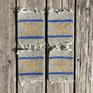 May include: Four gray woven coasters with blue and yellow stripes. The coasters have a frayed edge.