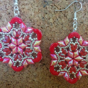 Può includere: Un paio di orecchini a forma di fiocco di neve rosso e argento. Gli orecchini sono fatti di piccole perline e hanno un design delicato e intricato.