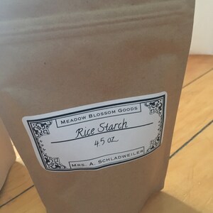 Peut inclure: Un sac en papier brun avec une étiquette blanche indiquant "Meadow Blossom Goods Rice Starch 4.5 oz MRS. A. SCHLADWEILER"