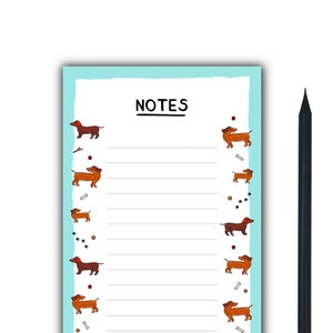 Puede incluir: Un bloc de notas azul con un interior blanco rayado y un borde de dachshunds marrones y huesos de perro. El bloc de notas tiene la palabra "NOTES" impresa en la parte superior.