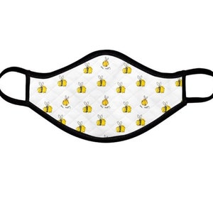 Può includere: Una maschera facciale bianca con un bordo nero e un motivo ripetuto di api gialle con il testo "Bee Happy" su di esse.