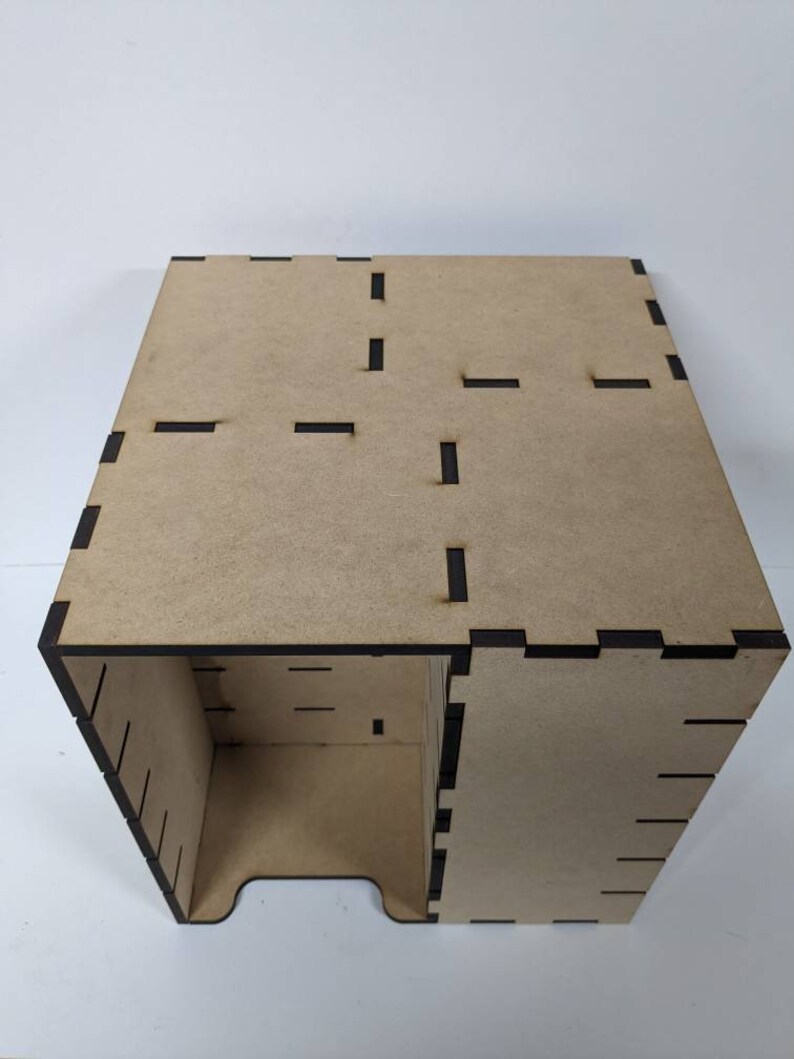 May include: A wooden box with a brown finish and black edges. The box has a series of slots cut into the sides and top.