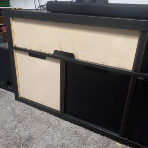 May include: A black and natural wood-toned media console with two drawers. The top drawer is natural wood, and the bottom drawer is black. A black soundbar sits on top of the console.