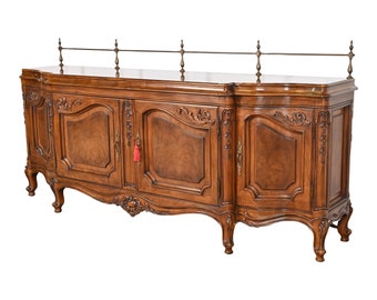 May include: A large, ornate wooden sideboard with four doors and a brass railing on top. The sideboard has intricate carvings and a rich brown finish.