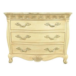 May include: Cream-colored three-drawer chest with ornate carvings and leaf-shaped drawer pulls. The top of the chest has a decorative trim. The chest has curved sides and decorative feet.