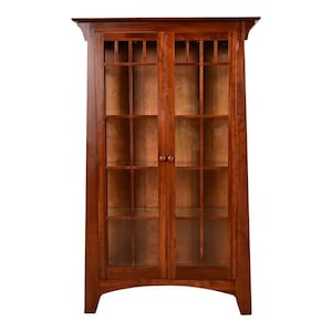 May include: A wooden display cabinet with two glass doors and a warm, reddish-brown finish. The cabinet features a rectangular shape with a slightly curved base and a decorative top. The doors have a grid pattern, and the cabinet is designed for storage.