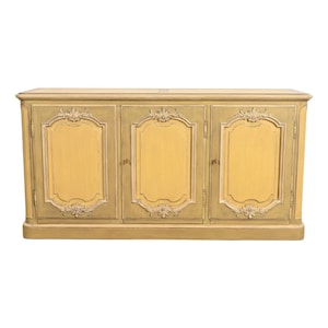 May include: A three-door cabinet with a light yellow and green painted finish. The cabinet doors are framed with ornate white trim and decorative floral accents. The cabinet is a classic furniture piece.