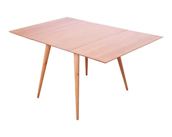 May include: A light wood folding table with four slender legs. The table top is made of three panels that can be folded to make the table smaller.