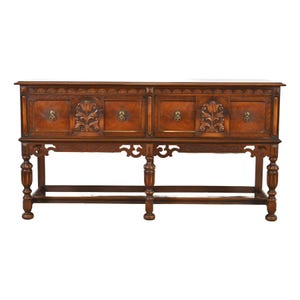 May include: A dark brown wooden sideboard with four drawers and ornate carvings. The drawers have brass knobs and floral designs. The sideboard sits on decorative legs and has a detailed top edge. A classic piece of furniture.
