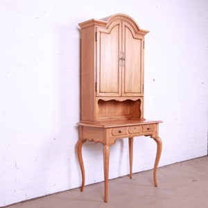 May include: A light wood desk with a hutch. The desk has a curved top and three drawers. The hutch has two doors and a shelf. The desk is in a white room.