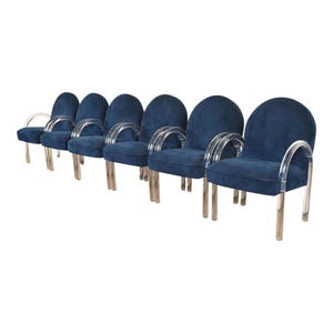 May include: Six blue velvet armchairs with clear acrylic armrests and chrome legs. The chairs have a rounded back and a low seat. The armrests curve gracefully from the back to the front of the chair.