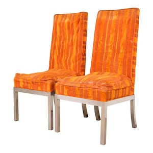 May include: Two orange and yellow striped upholstered chairs with stainless steel legs. The chairs have a high back and a square seat cushion. The fabric has a vertical stripe pattern in shades of orange and yellow.