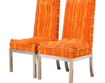 May include: Two orange and yellow striped upholstered chairs with stainless steel legs. The chairs have a high back and a square seat cushion. The fabric has a vertical stripe pattern in shades of orange and yellow.