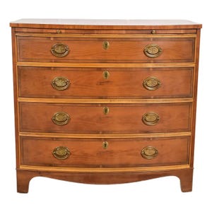 May include: A wooden chest of drawers with four curved drawers. The chest is made of light brown wood with brass hardware and decorative inlay. The drawers have keyholes and oval-shaped pulls.