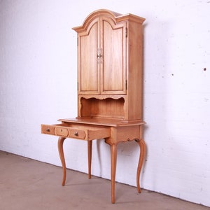 May include: A light wood desk with a hutch. The desk has two drawers and four legs. The hutch has two doors and a shelf. The desk is in a white room.
