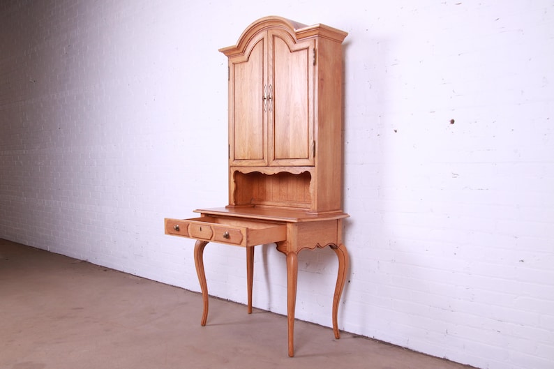 May include: A light wood desk with a hutch. The desk has two drawers and four legs. The hutch has two doors and a shelf. The desk is in a white room.