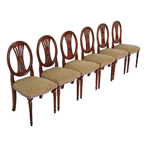 May include: Set of six antique wooden chairs with oval backs and patterned seats. The chairs have dark brown frames and legs, with a decorative carved design on the backrests. The seats are upholstered in a yellow, black, and white checkered fabric.