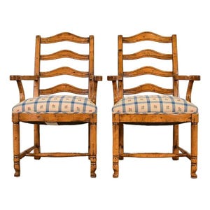 May include: Two antique wooden armchairs with ladder backs and plaid seat cushions. The chairs have a warm, honey-toned finish and curved armrests. The seat cushions feature a blue and white plaid pattern with small floral accents.