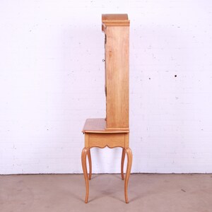 May include: A light wood desk with a hutch. The desk has a drawer and four legs. The hutch has glass doors and shelves.