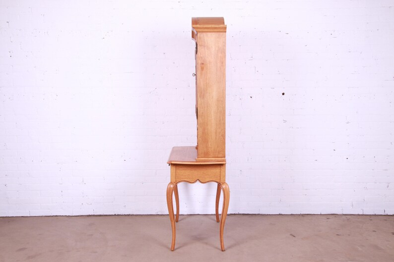 May include: A light wood desk with a hutch. The desk has a drawer and four legs. The hutch has glass doors and shelves.