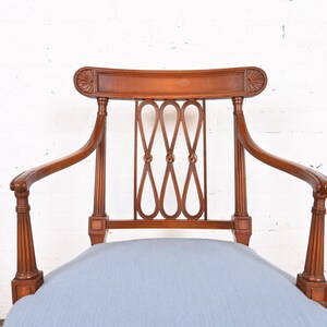 May include: A wooden armchair with a light blue cushion. The chair has a carved back and arms, and a woven design on the back.