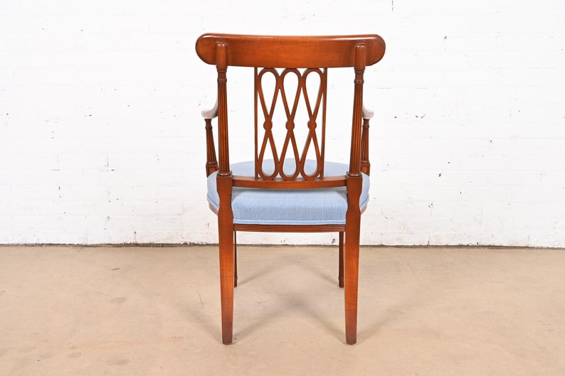 May include: A wooden armchair with a light blue fabric seat and a decorative back with a woven design. The chair has a rounded back and four legs.