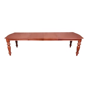 May include: A wooden dining table with a rectangular top and turned legs. The table is made of a light brown wood and has a natural finish.