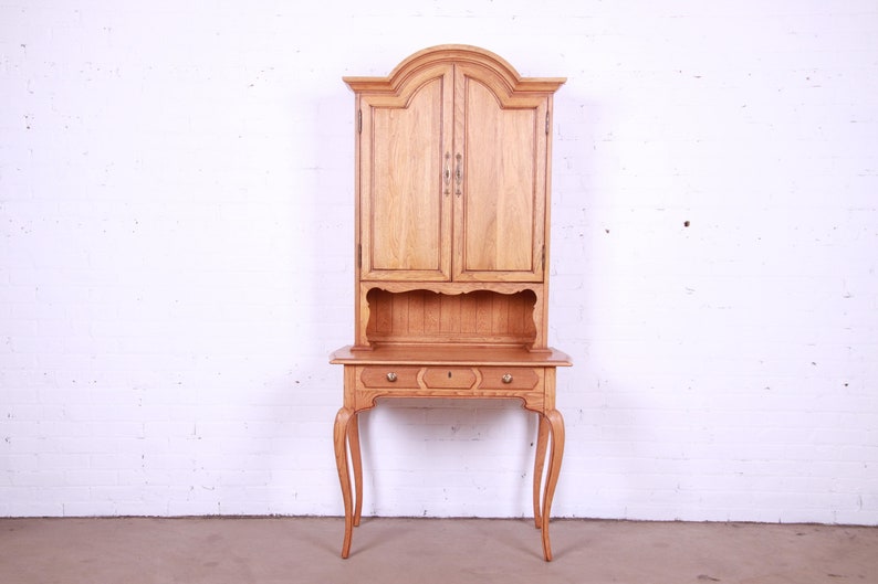 May include: A light wood desk with a hutch. The desk has three drawers and cabriole legs. The hutch has two doors and a shelf.