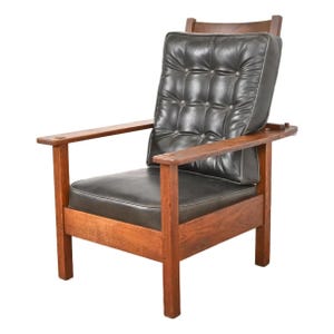 May include: A vintage armchair with a dark leather cushion and backrest. The wooden frame has a warm, reddish-brown finish. The chair features a button-tufted back and armrests, offering a classic and comfortable design.