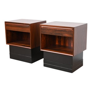 May include: Two matching wooden nightstands with a drawer and a shelf. The nightstands are made of dark wood with a black base.
