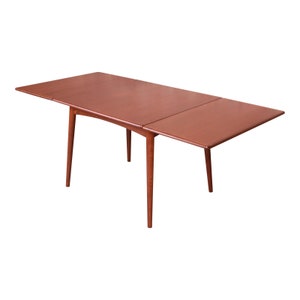 May include: A mid-century modern extendable dining table made of wood with a reddish-brown finish. The table has a rectangular top and four slender legs.