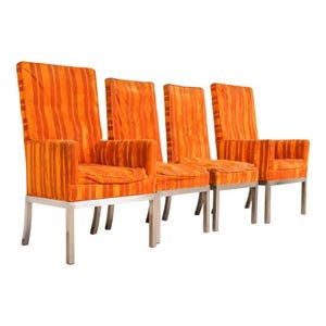 May include: Four mid-century modern armchairs with high backs. The chairs have orange and red vertical striped upholstery and chrome legs. The chairs have armrests and seat cushions. The chairs are set against a white background.