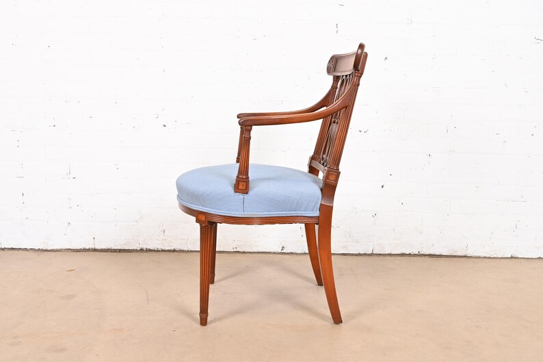 May include: A wooden armchair with a light blue upholstered seat and back. The chair has a carved design on the back and arms.